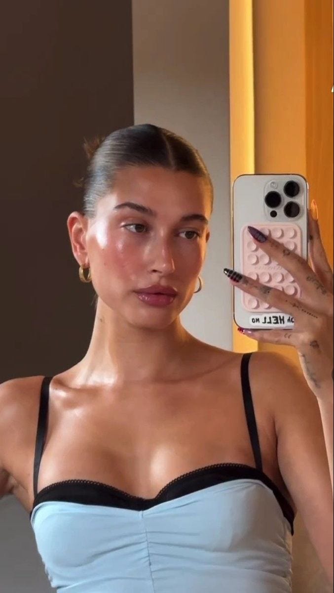 This may contain: a woman taking a selfie in front of a mirror with her cell phone and makeup brush