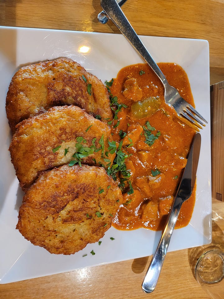 On the right, a plate of potato pancakes with a side of goulash; on the left, a glass of herbal tea in a mason jar.