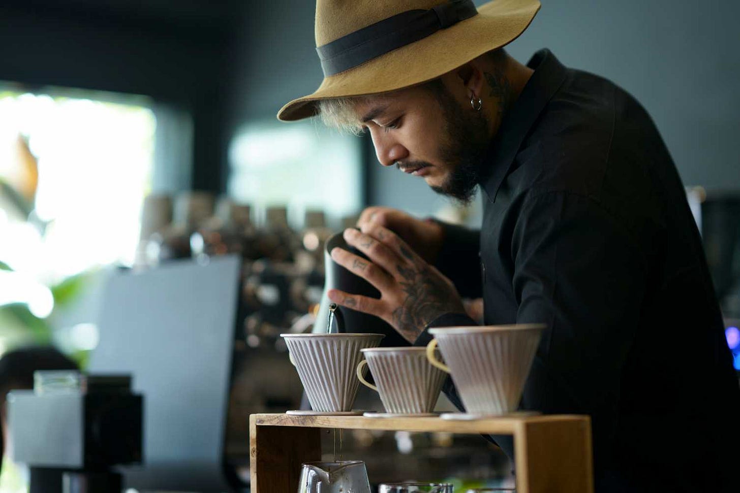 Barista with a beard and tattooed hands pours boiling water over coffee grounds. Barista with a beard and tattooed hands pours boiling water over coffee grounds.