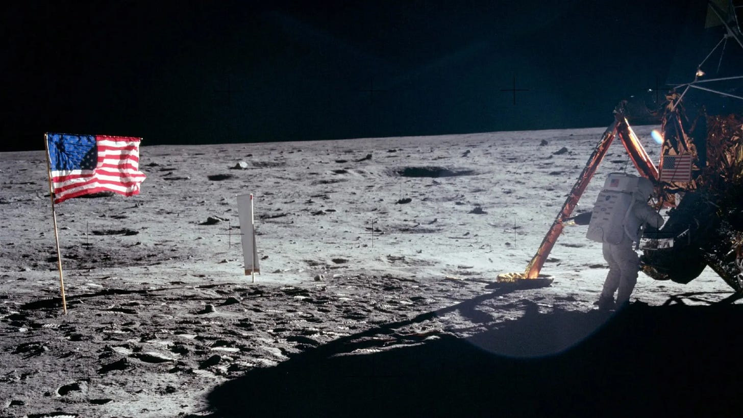 Apollo 11 astronaut on the lunar surface near the lunar module, with the American flag planted in the Moon’s soil under a dark sky.