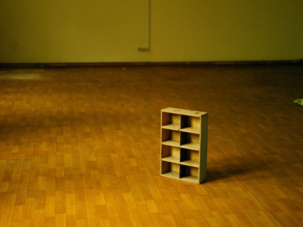 A miniature bookcase stands alone on a wooden floor in an empty room