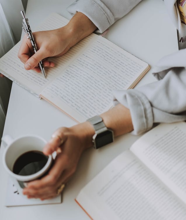 Free Person Writing on Notebook While Holding Coffee Mug Stock Photo