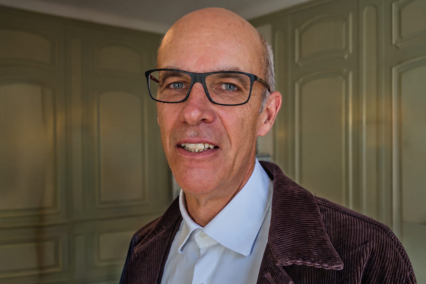 Porträt von Christof Dietler, einem lächelnden, kahlköpfigen Mann mit schwarzer Brille. Er trägt ein weisses Hemd und ein dunkelbraunes Cordjackett und steht vor der getäfelten Wand eines historischen Innenraums. Porträt von Christof Dietler, einem lächelnden, kahlköpfigen Mann mit schwarzer Brille. Er trägt ein weisses Hemd und ein dunkelbraunes Cordjackett und steht vor der getäfelten Wand eines historischen Innenraums.