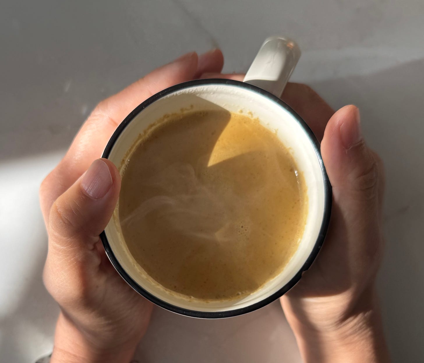Top-down view of a warm drink held with both hands; soft steam and sunlight. Top-down view of a warm drink held with both hands; soft steam and sunlight.