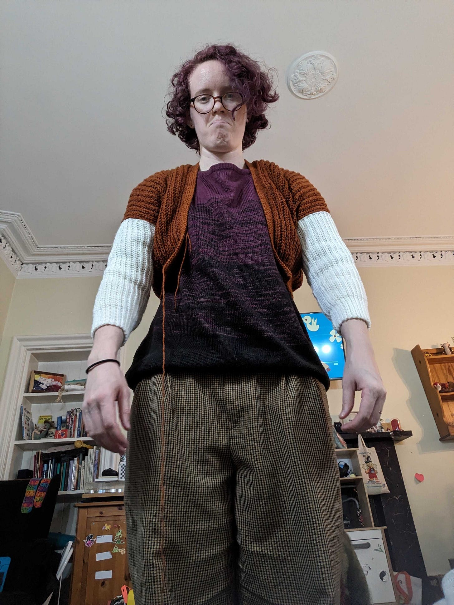 An image of Nicki wearing the cardigan they made that is about 2 sizes too small. Nicki is pouting and looking down at the camera.