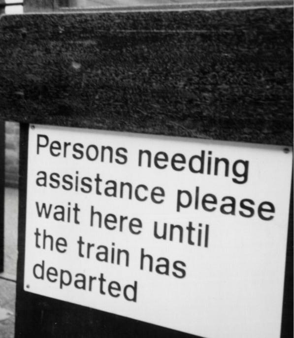 Old black and white photo of a sign saying Persons who need assistance please wait here until the train has departed