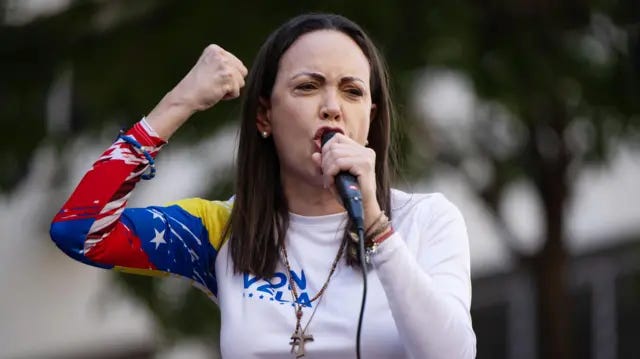 Maria Corina Machado con una mano empuñada y la otra sosteniendo un micrófono se dirige con vehemencia a quienes la escuchan mientras frunce el ceño. Maria Corina Machado con una mano empuñada y la otra sosteniendo un micrófono se dirige con vehemencia a quienes la escuchan mientras frunce el ceño.