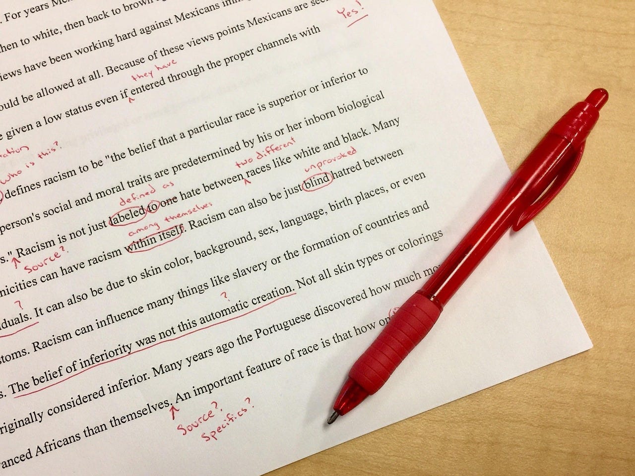 Photo of an essay on racism with red edits and a red ballpoint pen beside it, sitting on a light wooden surface