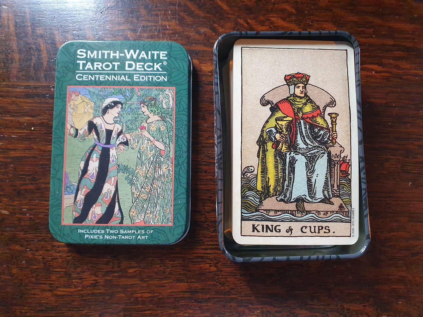 A closeup of the Smith Waite Tarot Deck Centennial Edition. The King of Cups sits at the top of the carrying tin that the cards are packaged in