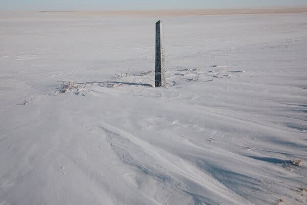 A short obelisk in an empty snow-covered field.