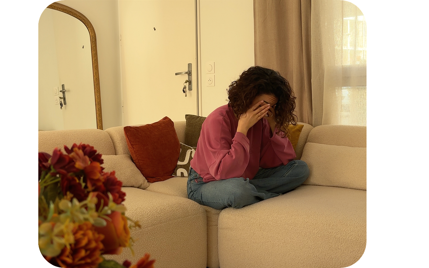 Une femme assise en tailleur sur un canapé clair, dans un salon aux tons chauds, se couvre le visage avec les mains comme dans un moment de fatigue ou de saturation. Une femme assise en tailleur sur un canapé clair, dans un salon aux tons chauds, se couvre le visage avec les mains comme dans un moment de fatigue ou de saturation.