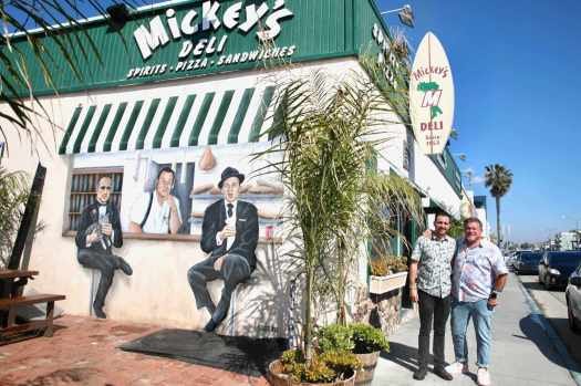 Mickey Mance and his father, Paul stand outside Mickey’s Deli in Hermosa Beach on Friday, Mar. 31, 2023. A mural on the patio  depicts family patriarch, Michael Angelo “Mickey” Mance, who opened the business in 1953, in between Marlon Brando and Frank Sinatra. (Photo by Howard Freshman, Contributing Photographer)
