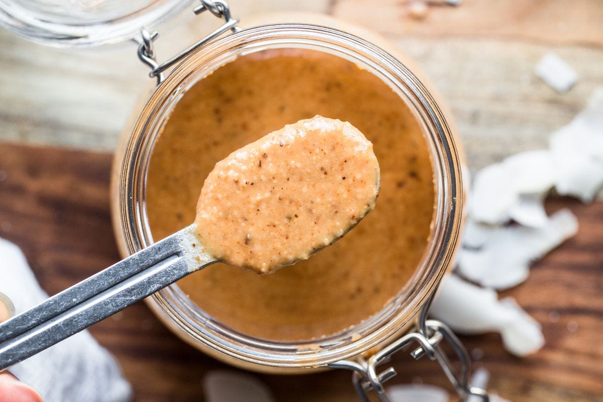 Overhead shot of a jar of homemade coconut butter with a hand spooning out a spoonful. Overhead shot of a jar of homemade coconut butter with a hand spooning out a spoonful.