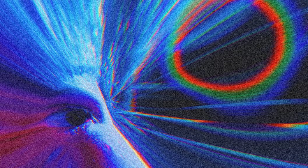 close em um rosto, na parte do olho direto, mas a imagem e distorcida e a única coisa que se distingue é o olho. Há um reflexo colorido ao lado, as cores são frias, e há algo de muito estranho na imagem