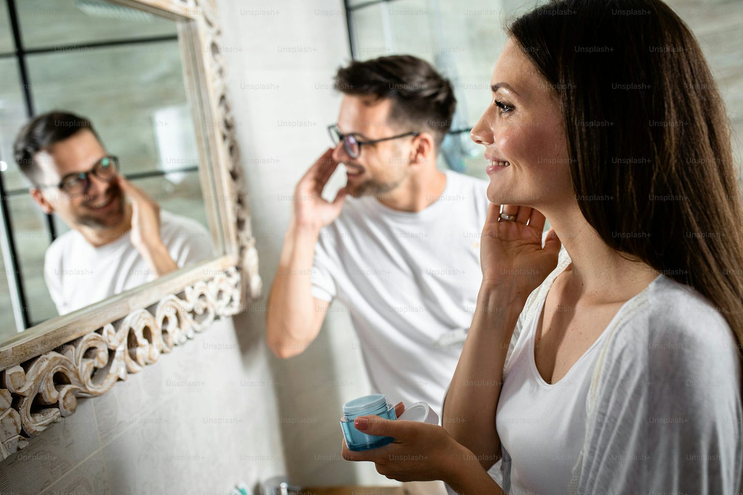 Pareja joven que realiza la rutina matutina en el baño aplicándose crema facial.