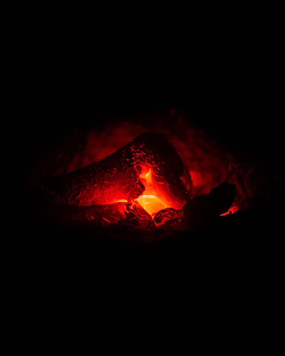 A glowing ember surrounded by dark charcoal, radiating deep red and orange light in darkness A glowing ember surrounded by dark charcoal, radiating deep red and orange light in darkness