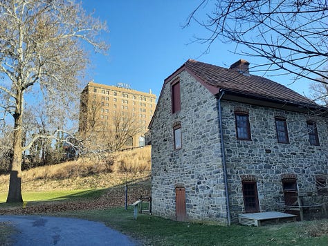 Pictures from Bethlehem, Pa., starting with the oldest waterworks in the United States, built in the 1700s. It's a stone building with cloudy sky. Next picture is three carriage horses standing in front of the 9-story tall brick Hotel Bethlehem, and a historic stone building that was used as a hospital during the Revolutionary War. Middle row is the Sun Inn Tavern, where almost all of our Founders ate and gathered at one time or another, The building is stone and there is white picket fence in the back and a porch with a red, white and blue banner on the side. Bottom row: Bethlehem's industrial park with original buildings made of stone against a blue sky. Last photo is the blacksmith busy at work in the blacksmith shop with a blazing fire.