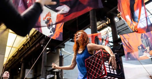 A woman holding a milk crate underneath her arm.