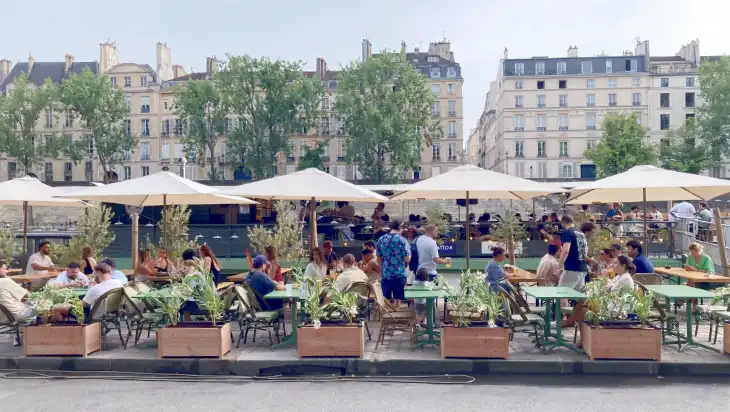 Photo of people sitting at a riverside terrace in Paris. Photo of people sitting at a riverside terrace in Paris.