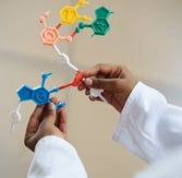 A researcher of the global majority in a lab coat holding a model of DNA.