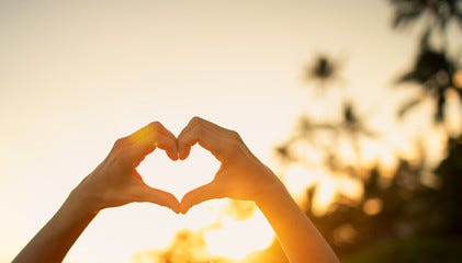 Hand making heart shape on beautiful sunset background. 