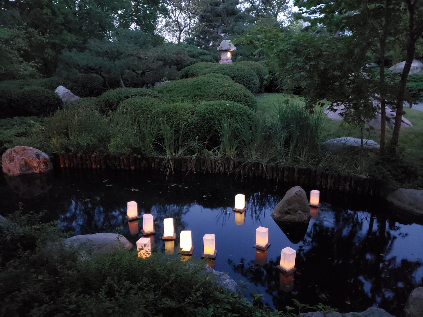 Lit floating lanterns are in the water of the Japanese Garden with the stone lantern lit in the background.