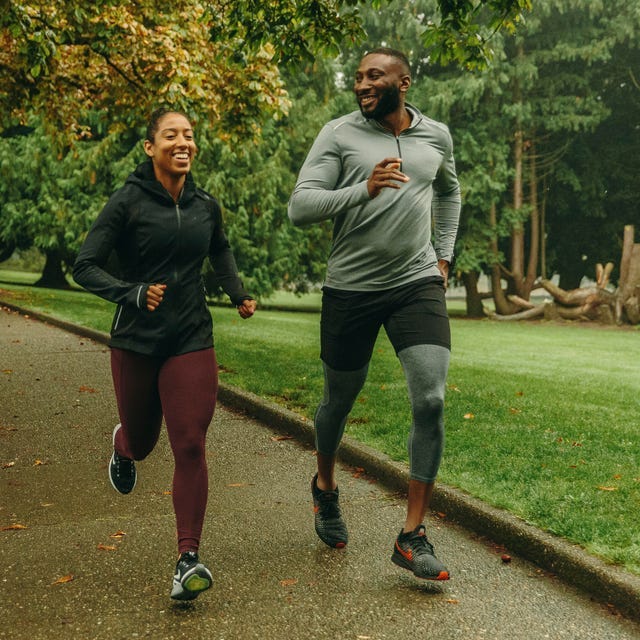 Two people jogging together on a park path surrounded by green trees. Two people jogging together on a park path surrounded by green trees.