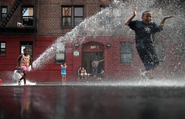 This may contain: children play in the water spouting from a fire hydrant on a city street