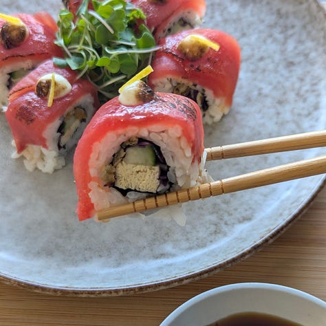 Three types of plant-based uramaki sushi rolls, each topped with colorful ingredients. The rolls have rice on the outside and are sliced into bite-sized pieces.