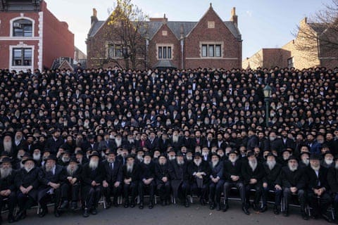 a large group of bearded men in black clothing and hats in front of a red brick building