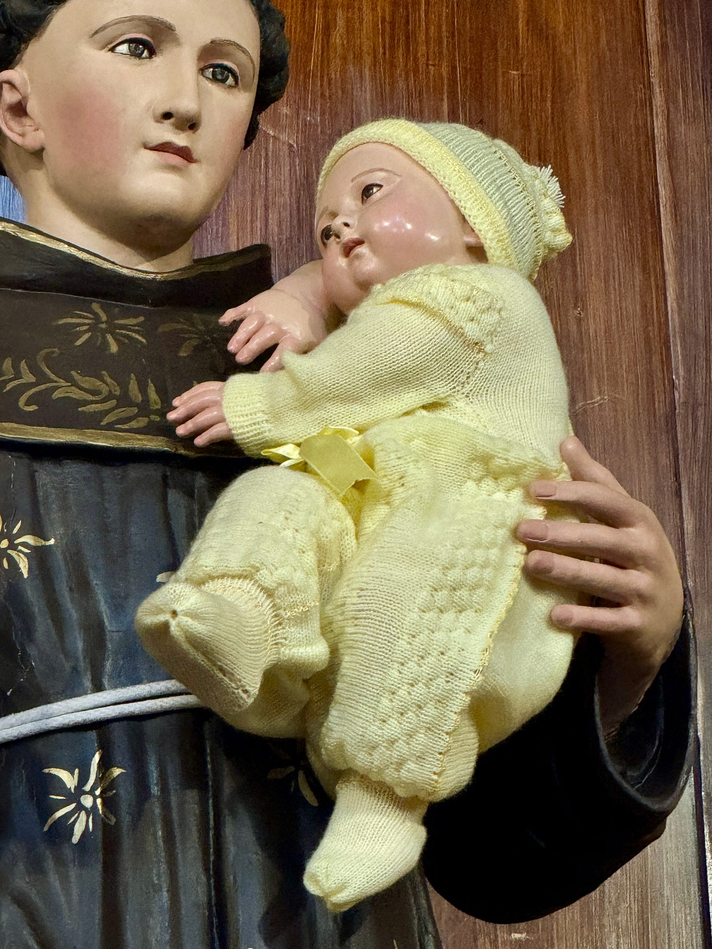 Niño Jesús en brazos de San Antonio vistiendo ropa de bebé.
