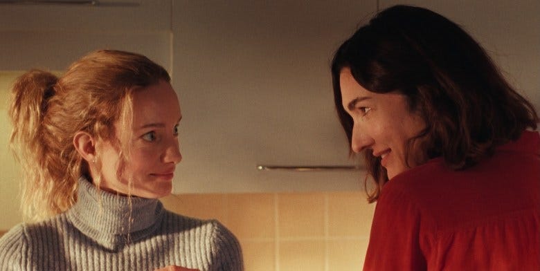 Actors Laurence Leboeuf and Karine Gonthier-Hyndman look at each other with conspiring smiles in a still from the movie "Two Women." 