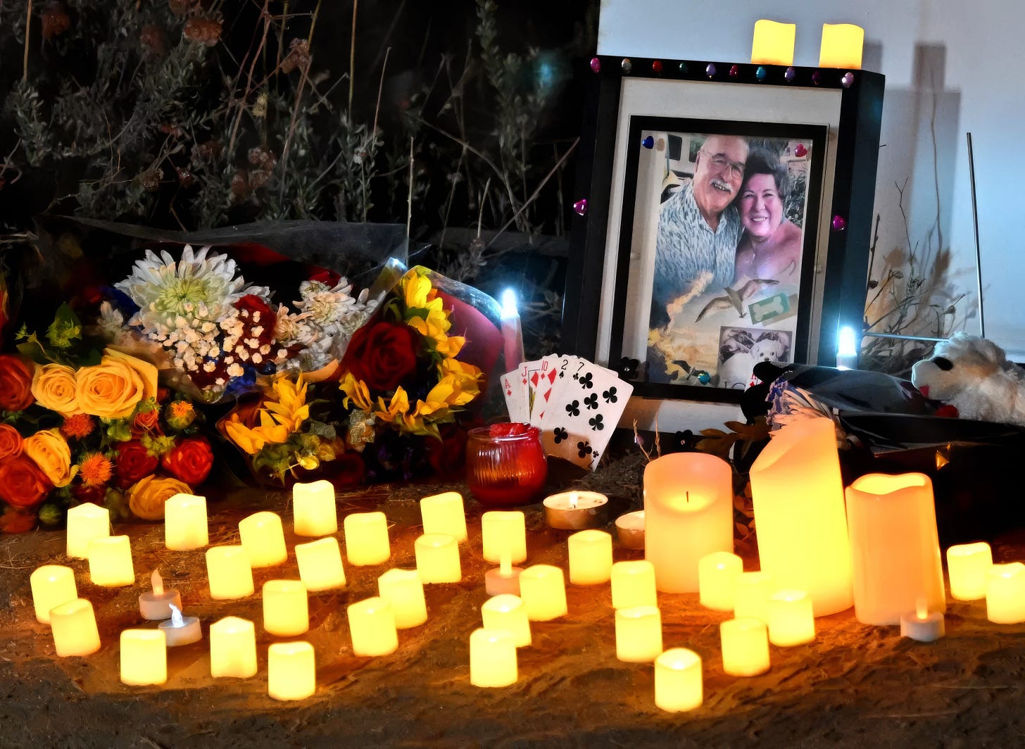 A framed photo of Daniel and Stephanie Menard lit by several candles beside flowers in their memory.
