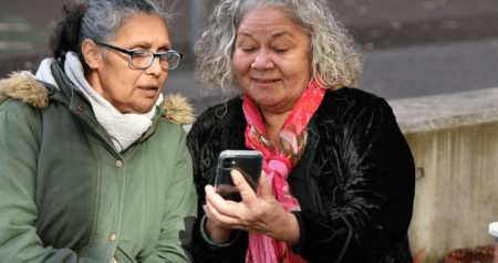 Two Indigenous women with grey hair are looking at a smart phone.with 