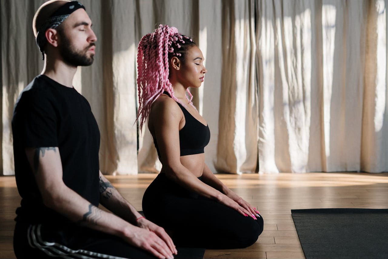 A man and a woman dressed in black sit in meditation with their legs under their body and their hands on their knees. A man and a woman dressed in black sit in meditation with their legs under their body and their hands on their knees.