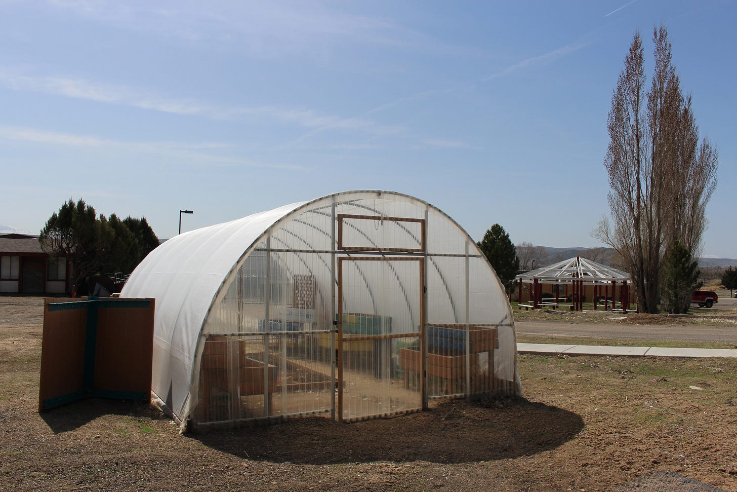 A photo of a hoop house, a structure similar to a greenhouse, with rounded hoops supporting the structure and clear tarps trapping heat inside of it for growing plants. A photo of a hoop house, a structure similar to a greenhouse, with rounded hoops supporting the structure and clear tarps trapping heat inside of it for growing plants.