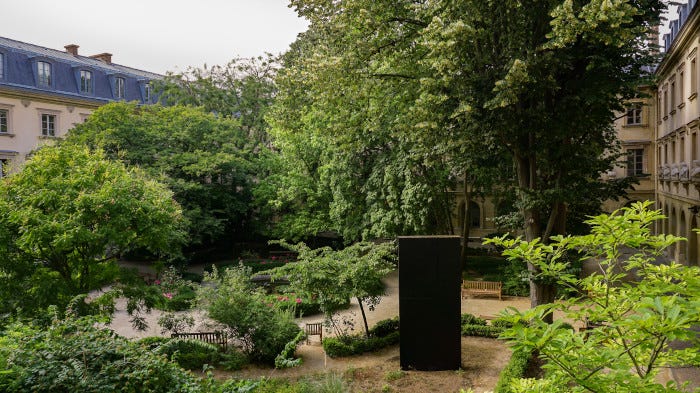 Picture of peaceful garden containing a tall, black, rectangular monolith. 