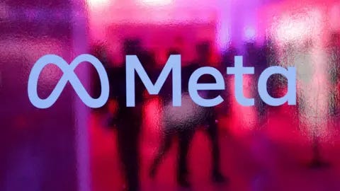 Reuters Meta's logo is displayed against pink, frosted glass. Behind the logo are the silhouettes of people. 
