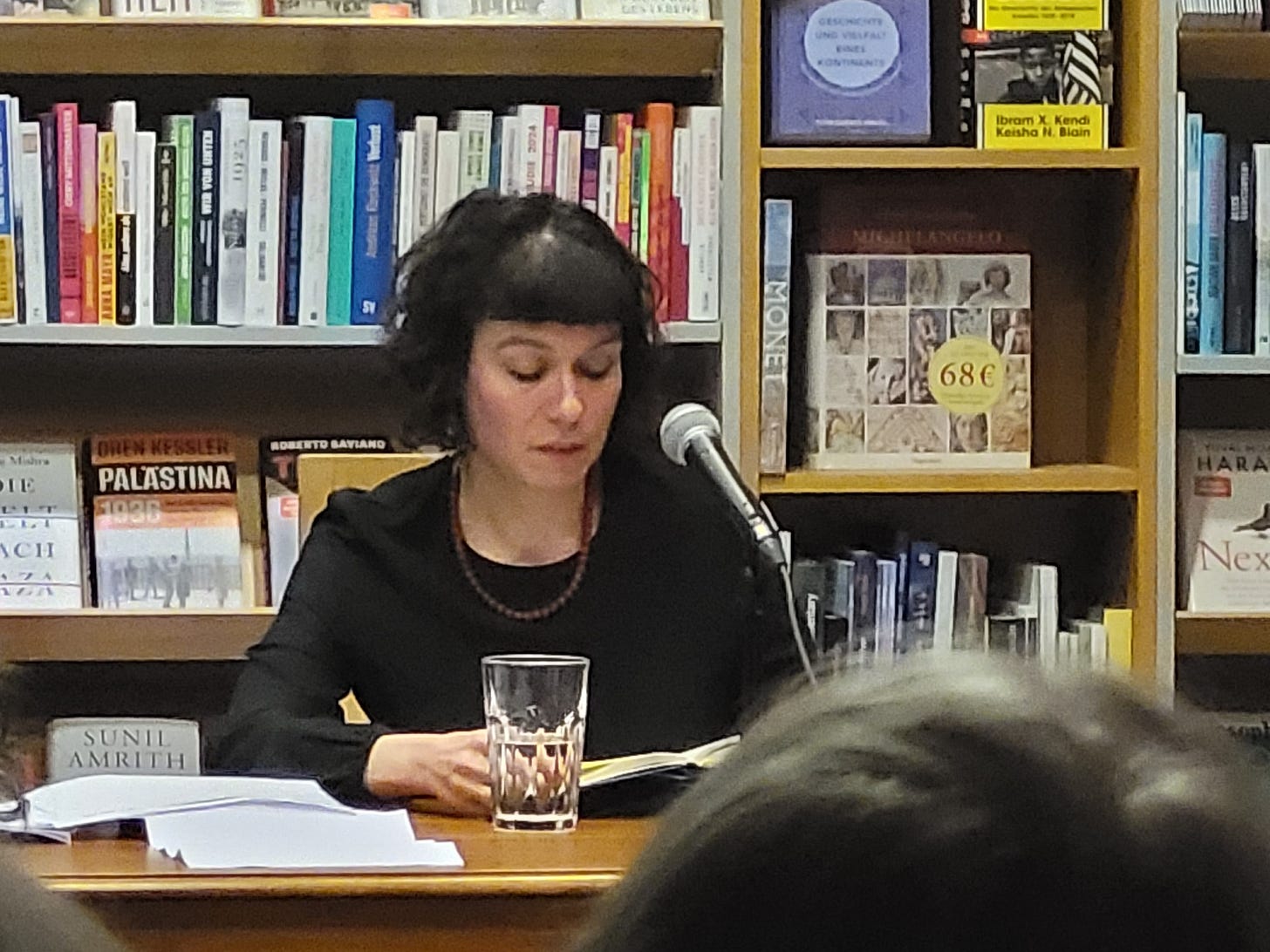 In dunkler Kleidung sitzt Sarah Lorenz vor einem Bücherregal in der Freiburger Buchhandlung Schwarz und liest aus ihrem Roman „Mit dir, da möchte ich im Himmel Kaffee trinken“ vor. (Bild: vliestext)