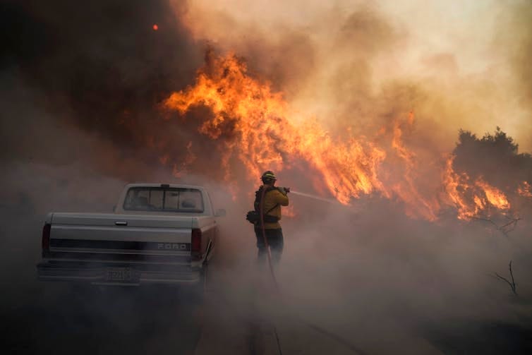 A firefighter holds a fire hose shooting water at a wall of flames burning along a road near Irvine, California, in 2020. A firefighter holds a fire hose shooting water at a wall of flames burning along a road near Irvine, California, in 2020.