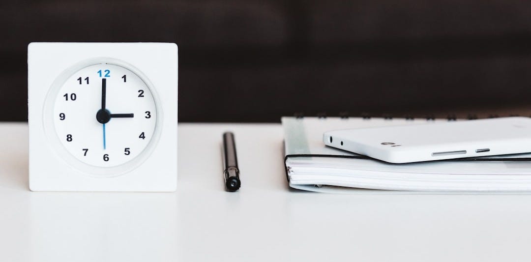 white desk clock near pen and book