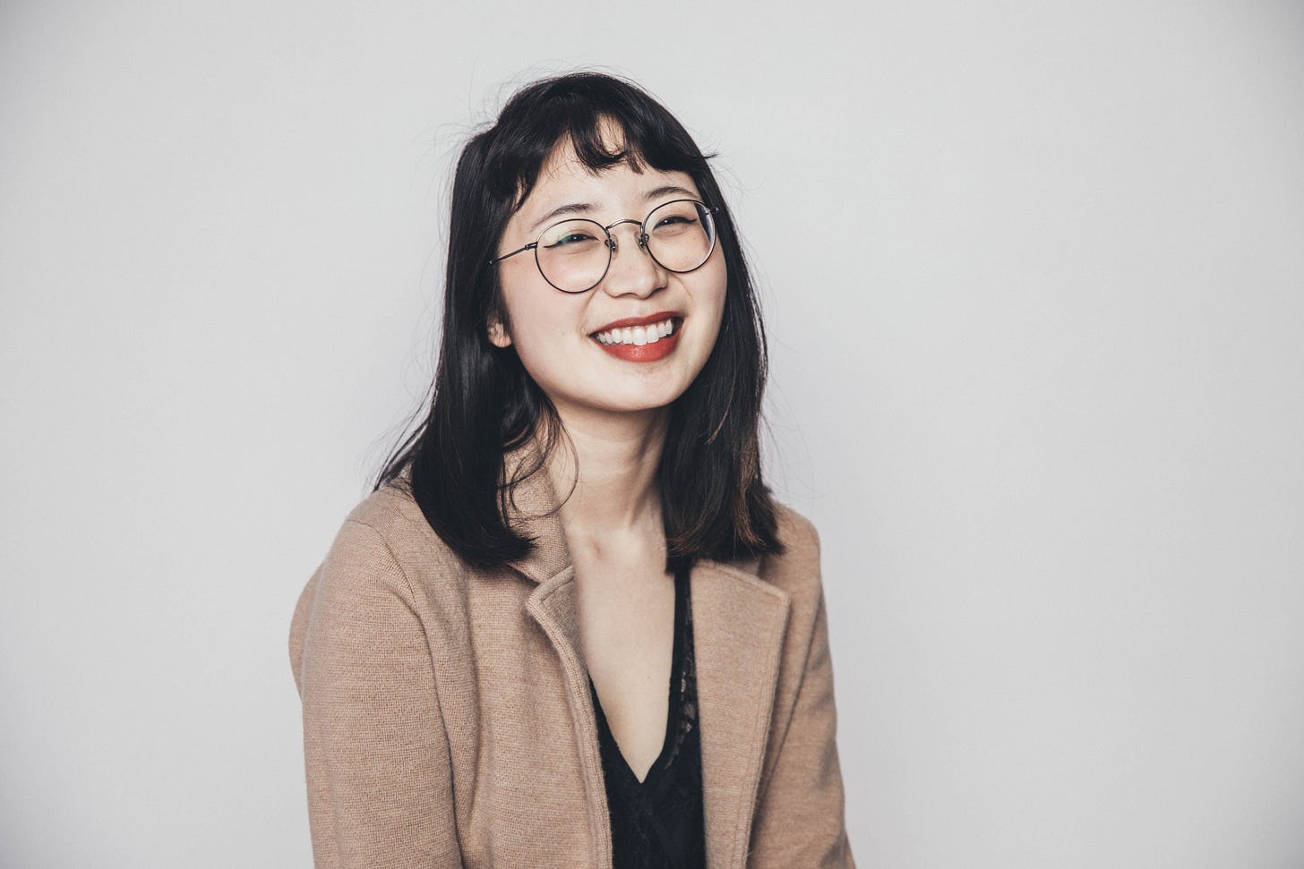 Tiffany in brown blazer sitting, smiling, and posing in front of a blank background.