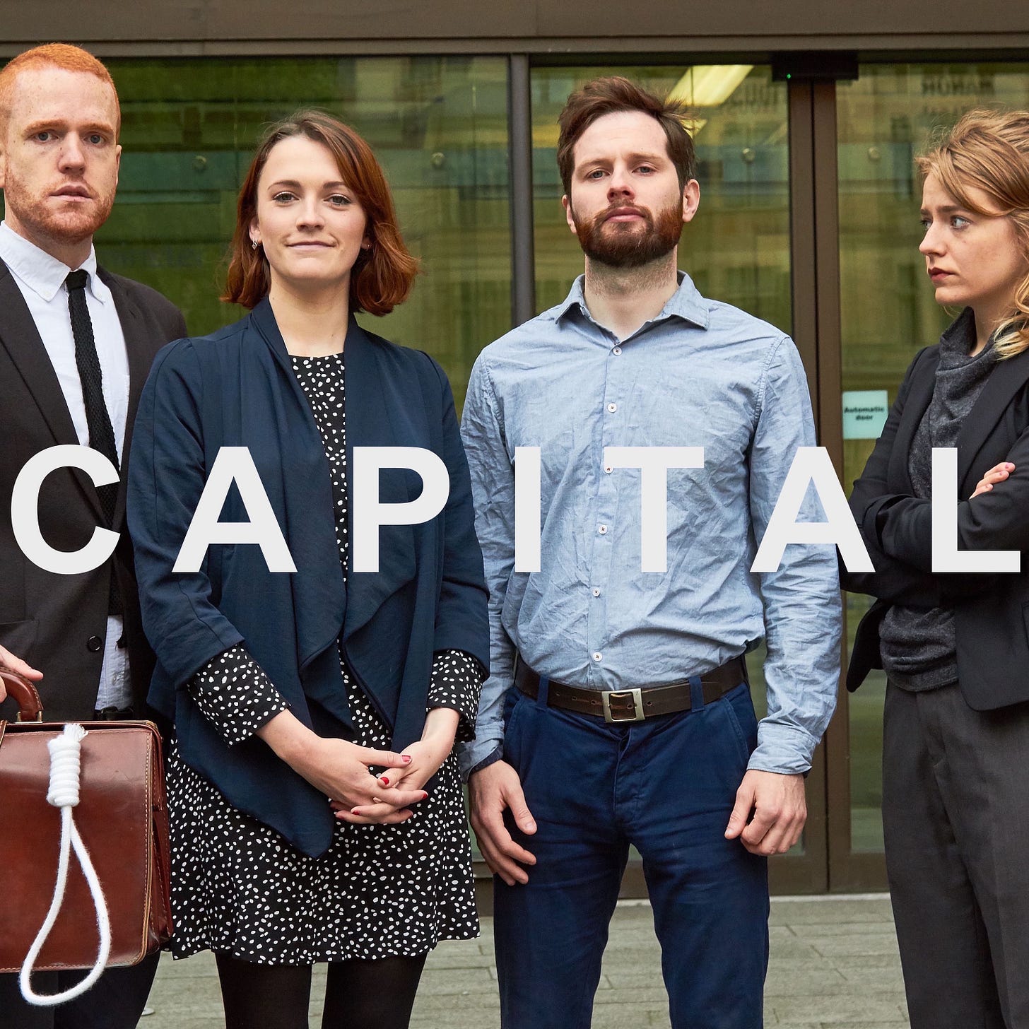 Artwork van CAPITAL. Het is een foto waarop je de vier comedians buiten voor een gebouw ziet staan. Van links naar rechts een man in pak met kort rossig haar, een vrouw met halflang bruin haar en een blauw jasje aan, een man met bruin kort haar en een baard en een blauw overhemd en een vrouw met blond haar in een zwart vrouwenpak. Eroverheen staat in witte letters de titel CAPITAL.