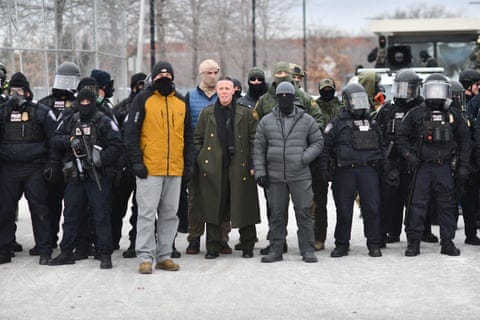 people in tactical gear and civilian clothing stand in a group outside