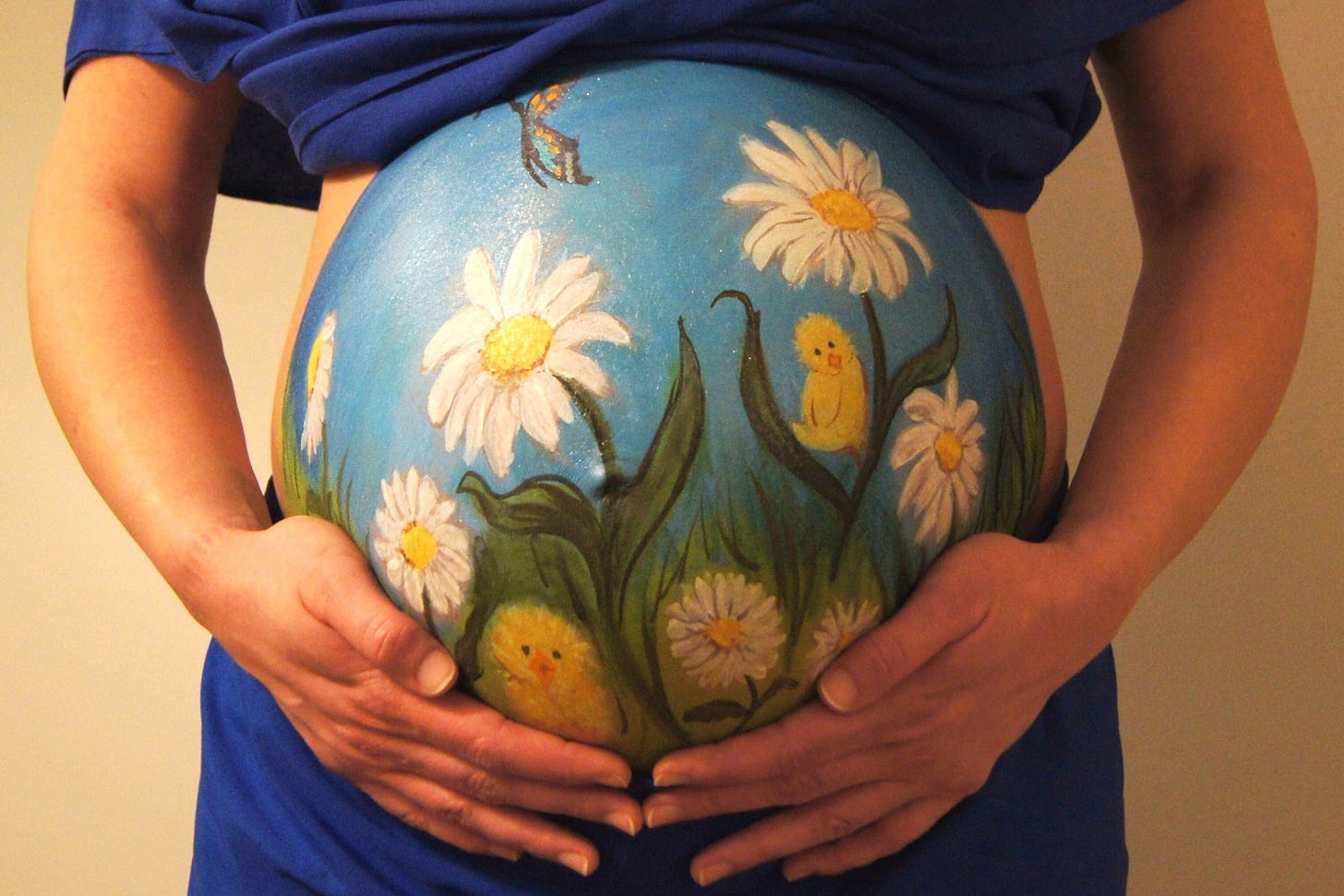 Pregnant woman cradling belly that is painted blue with daisies and butterflies Pregnant woman cradling belly that is painted blue with daisies and butterflies