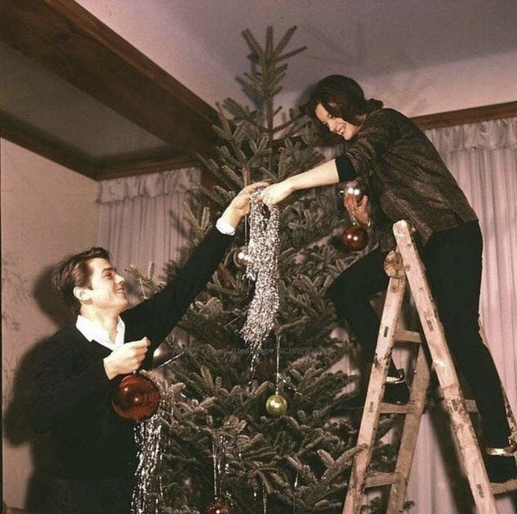 This may contain: two people are decorating a christmas tree