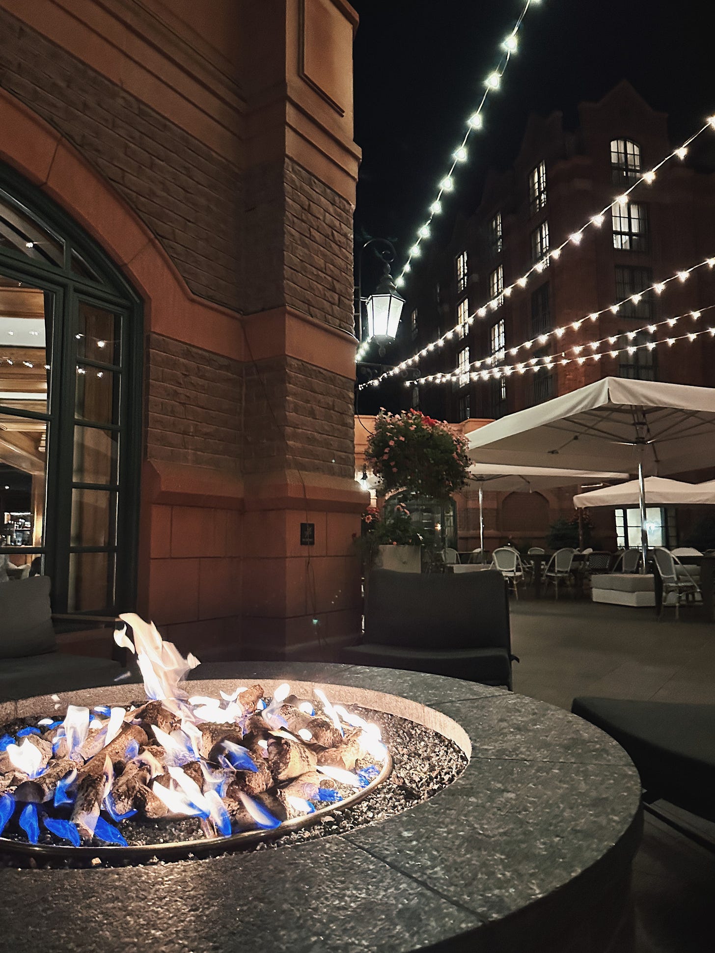 Outdoor fire pit glowing beneath rows of string lights in the St. Regis Aspen courtyard at night.