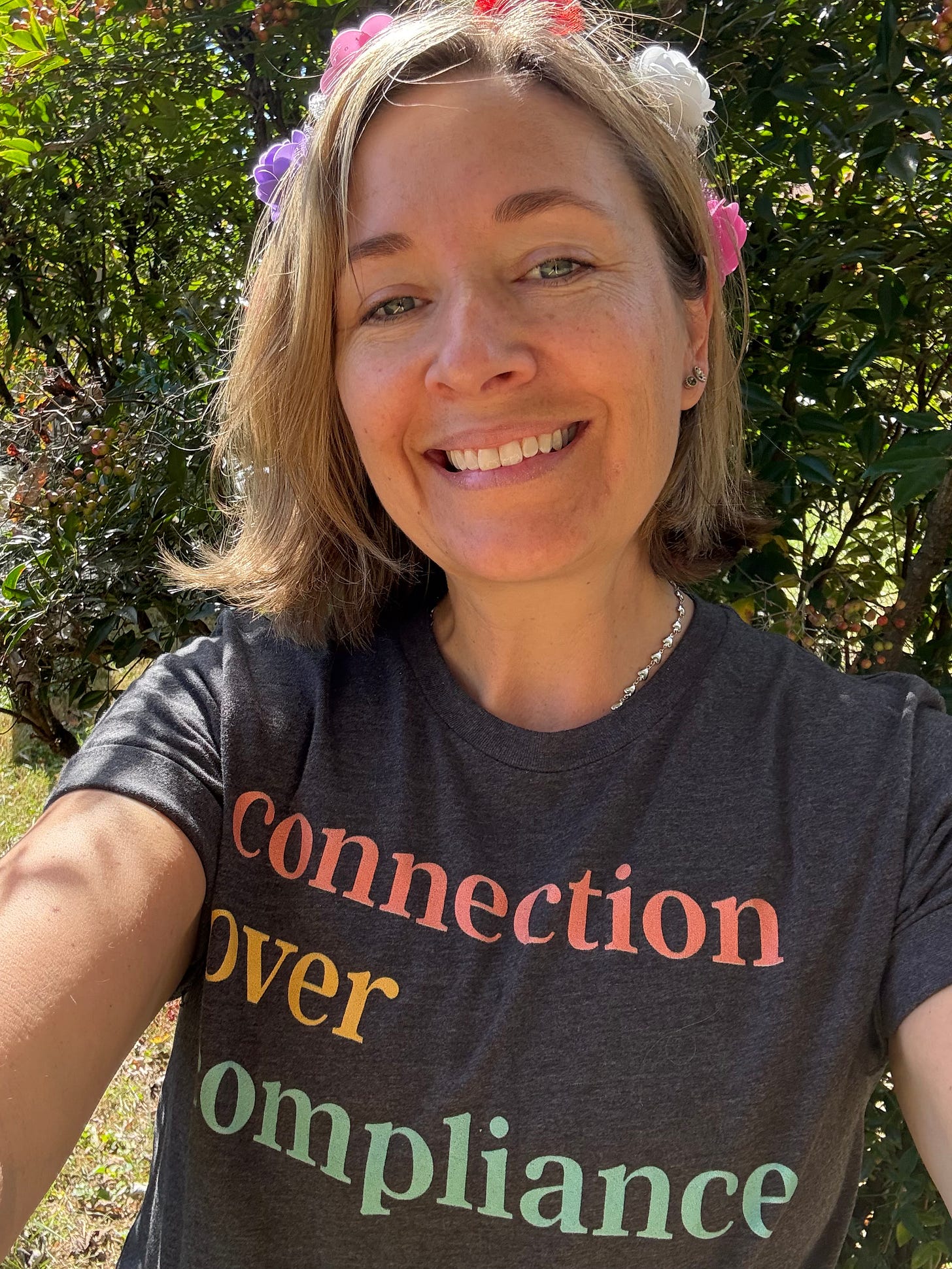 photo of me smiling with a flower crown and a tee shirt that reads, "connection over compliance"