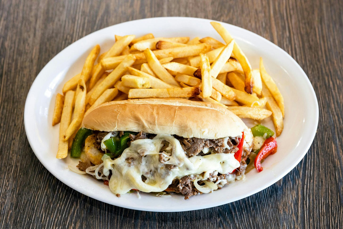A Philly cheesesteak with fries on a plate.