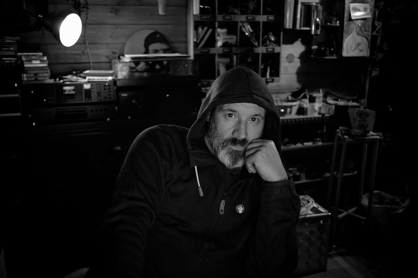 A photo of me in a hoody wondering if my camera that is resting on top of the monitor will fire after a short countdown.